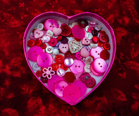 Heart Shaped Box Full of Pink, Red and White Buttons on a Red Backgroundの写真素材