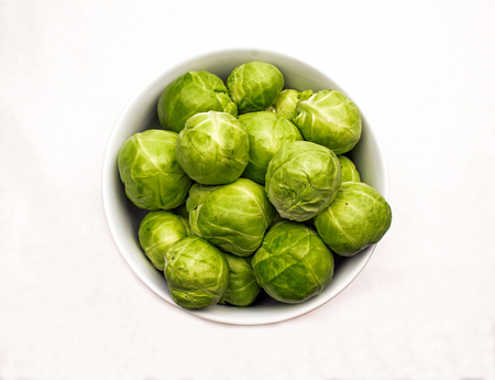 Closeup of a White Ceramic Bowl of Fresh Green Brussels Sprouts on a white backgroundの写真素材