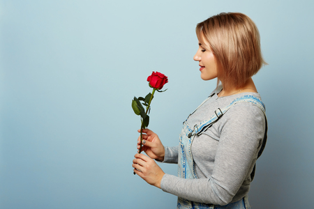 Beautiful girl in the overalls with red roses in hands on a blue background. Womens hands are holding a bouquet of rosesの写真素材