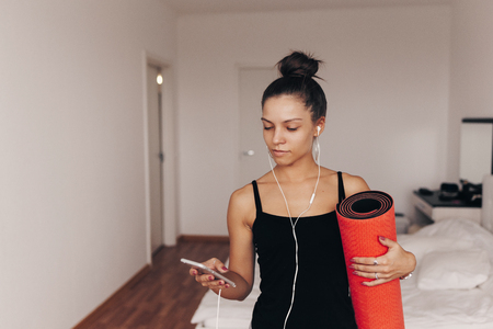 Happy attractive young woman holds in hands red yoga or fitness mat after working out at home in living room. Healthy life, keep fit conceptsの写真素材