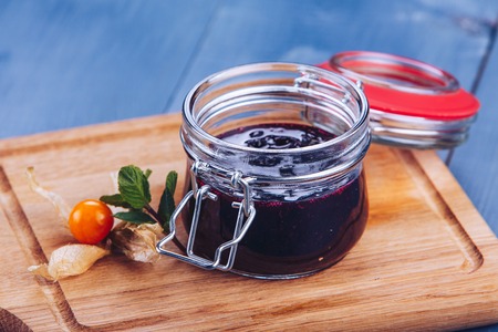 Berry jam. Glass jar of berry jam on blue background. Preserved fruits. Homemade berry jam in jar...