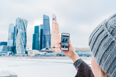 A girl is taking pictures on a mobile phone of a business center building. Moscow City International Business Center in Russiaの写真素材
