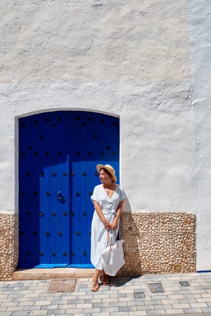 Fashion and lifestyle concept - beautiful woman in hat enjoying summer outdoors. European street old city.の写真素材