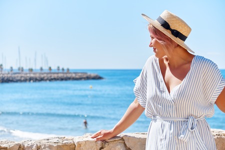 Beautiful girl in a summer dress and hat on the seashore near a background old city europe. Mediterranean Sea, Sitges, Spainの写真素材