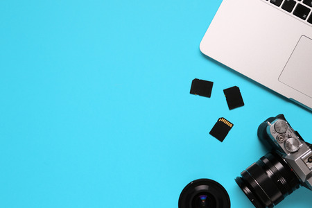 Top view of a desktop of a photographer consisting on a camera, a laptop, a notebook and a memory card on a blue desk background - copy spaceの写真素材