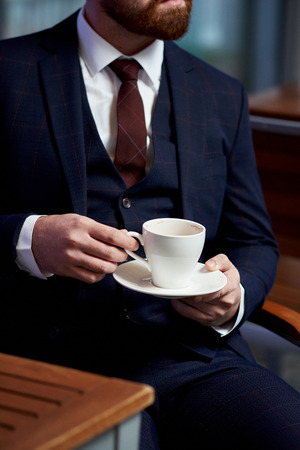 Business style. Men style. Businessman in a blue jacket with a cup of coffee in the cafe at the table, close-up.の写真素材