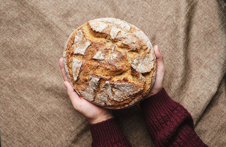 Woman Hand Holding Brown Bread Top Down View. Baked Whole Rye Grain Homemade Round Loaf on Rustic...
