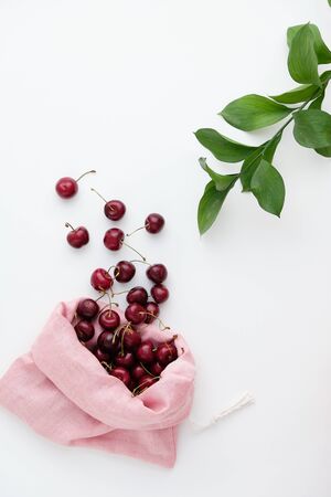 Organic Fresh Ripe Red Cherry Spilled Out from Bag Isolated on White Background and Decorated Green Leaves Branch Top View Copy Space. Heap of Agricultural Juicy Natural Sweet Eco Fruitの写真素材