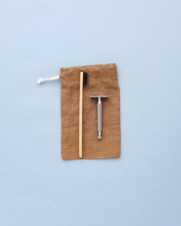 Toothbrush and Vintage Metallic Shaver on Pouch Isolated on Blue Background Copy Space Flat Lay. Bath Accessory Lying on Brown Color Textile Fabric Little Bag. Everyday Using Care Itemsの写真素材