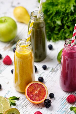 Bottle Healthy Fresh Fruit and Vegetable Smoothie Set Standing on White Table Black Wall Background. Different Taste Drink in Glass Container on Wooden Desk with Orange Pomegranate Seeds and Mint