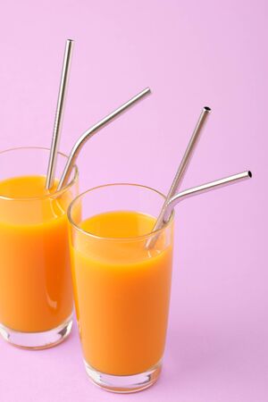 Two Orange Juice Glass with Metallic Steel Tubes Isolated on Purple Background Copy Space Photo. Alcohol Free Healthy Vitamin Fresh Drink. Tropical Beverage for Breakfast Standing on Violet Areaの写真素材