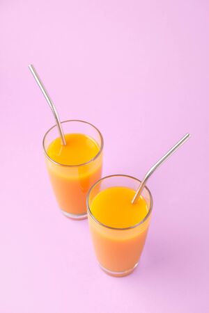 Two Orange Juice Glass with Metallic Steel Tubes Isolated on Purple Background Copy Space Photo. Alcohol Free Healthy Vitamin Fresh Drink. Tropical Beverage for Breakfast Standing on Violet Areaの写真素材