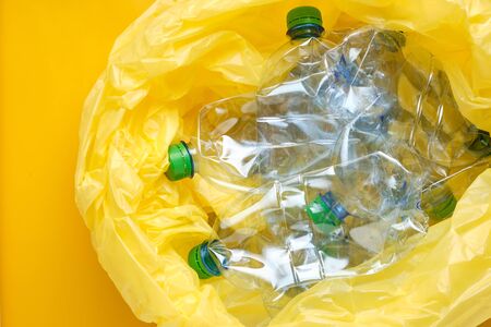 Plastic package with plastic bottles on yellow background. Recycling concept. Crushed PET bottles