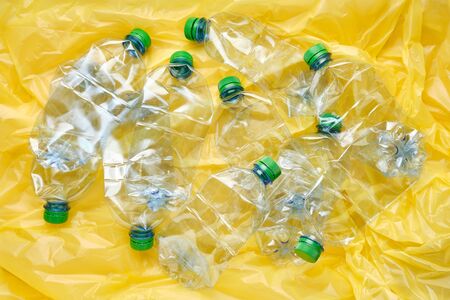 Used plastic bottles of water with caps on yellow background. Reの写真素材