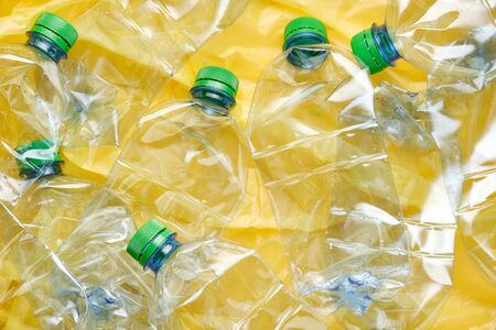 Used plastic bottles of water with caps on yellow background. Recycling concept. Crushed PET bottlesの写真素材