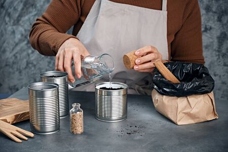 Young woman sowing seeds in metal cans.