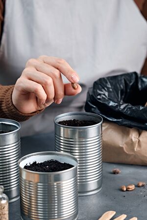 Young woman sowing seeds in metal cans.