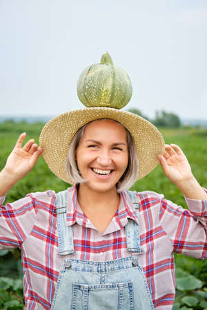 Woman Holding Green Fresh Pumpkin on Plants Field. Beautiful Young Girl with Healthy Vegetable Food Standing on Farm in Sunny Warm Day. Cultivation Vegan Culture Organic Nature Productの写真素材