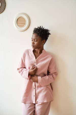 Young mysterious girl at dawn in a beautiful cozy gently pink muslin pajamas stands against a white wall. Cozy and comfortable. Front view.の写真素材