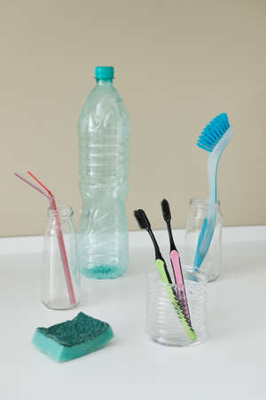 Plastic not eco-friendly home items. Environmental pollution. Waste problem, synthetic products in the environment. Front view of empty plastic bottle, dishwashing sponge, plastic disposable straws, plastic toothbrushes and plastic dishwashing brush.の写真素材