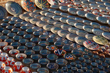 Many handmade plates and cups are laid out in a row at the bazaar in Uzbekistan. Plates and cups with different traditional ornaments. View from above.の写真素材