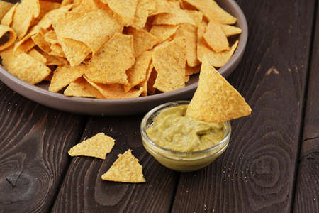 Nachos in a brown plate with guacomole on a dark brown wooden background. Mexican food concept,...