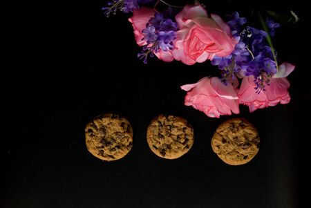 Pink autumn roses and violet flowers in a black background with cookiesの写真素材