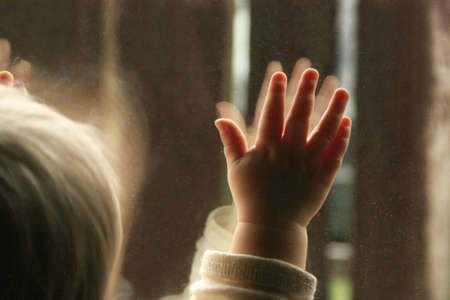 A little baby looking trough the window. Waiting for the end of quarantine isolation, longing to go outside. Father's day celebration indoors.の写真素材