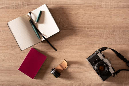 Top view of a retro analog camera, a negative spool, a passport and a notebook on a wooden table with copy space.の写真素材