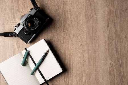 Top view of an analog vintage camera, a notebook and a pen on a wooden table with copy space.の写真素材