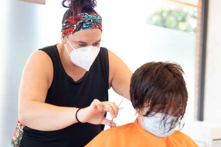 Working during covid-19 or coronavirus concept. Closeup frame of a professional hairdresser cutting the hair to a client with a face mask.の写真素材