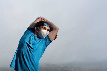 Closeup portrait of a young runner stretching with a medical face mask during the Covid-19 or...