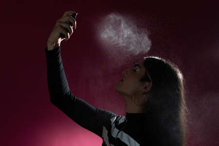 Studio shot with pink background of a young man putting on makeup. Applying make-up fixerの写真素材