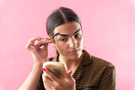 Studio portrait with pink background of a young man putting on makeup.の写真素材
