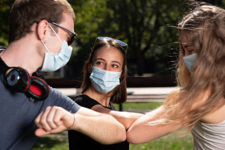 Three young friends greeting using their elbows and wearing face masks during Coronavirus or Covid-19 pandemic.の写真素材