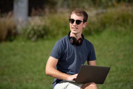 Handsome smiling blond teenager boy working on his computer outdoorsの写真素材