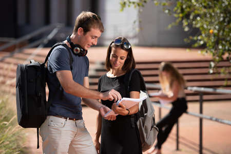 Young smiling college students wearing backpacks working on a notebook outdoor in the campus.の写真素材