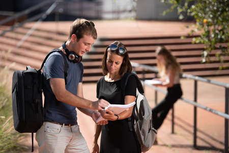 Young college students wearing backpacks working on a notebook outdoor in the campusの写真素材