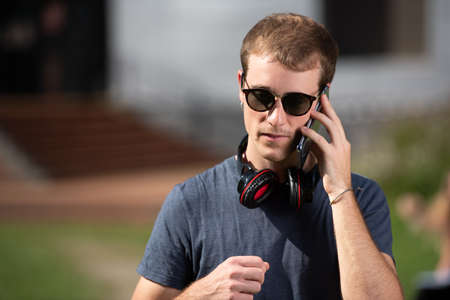 Portrait of a good looking handsome blond student boy wearing sunglasses and talking on the phone.の写真素材