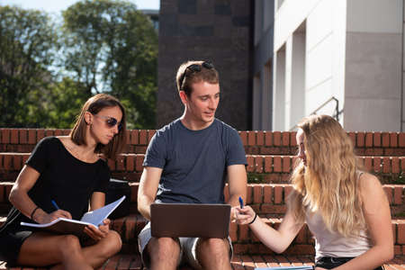 Young college students working together in a project with a laptop while sitting on the stairs.