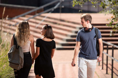 A couple of lesbian students walking together holding hands while a surprised skeptical boy is looking at them.の写真素材