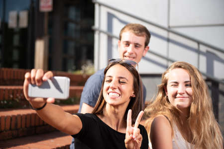 Three happy college students smiling and taking a selfieの写真素材