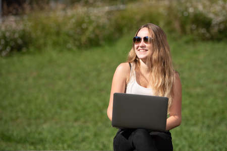 Portrait of a pretty smiling teenager girl working on her laptop with a green backgroundの写真素材
