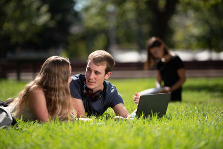 A couple of college students chatting laying on the ground of the campus park.の写真素材