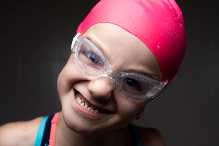 Closeup portrait of a little swimmer girl making faces to the camera with dark background.の写真素材