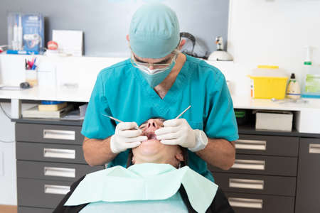 Dentist wearing double mask making a basic check up to a female patient during coronavirus pandemic.の写真素材