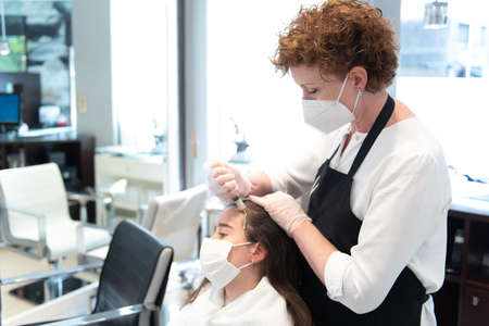 Working during Coronavirus pandemic concept. A hairdresser applying a treatment to a teenager client...