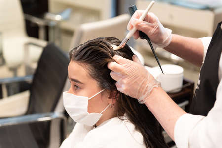 Working during Coronavirus pandemic concept. A female teenager patient getting a hair treatment with...