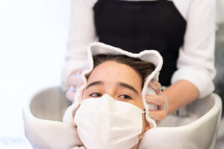 Working during Coronavirus pandemic concept. Coseup view of a teenager client wearing a mask getting the hair dried with a towel.の写真素材