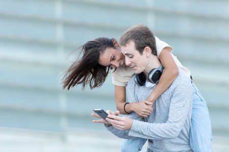 A happy smiling young couple hugging and checking a smartphone. Man carrying girl on the back.